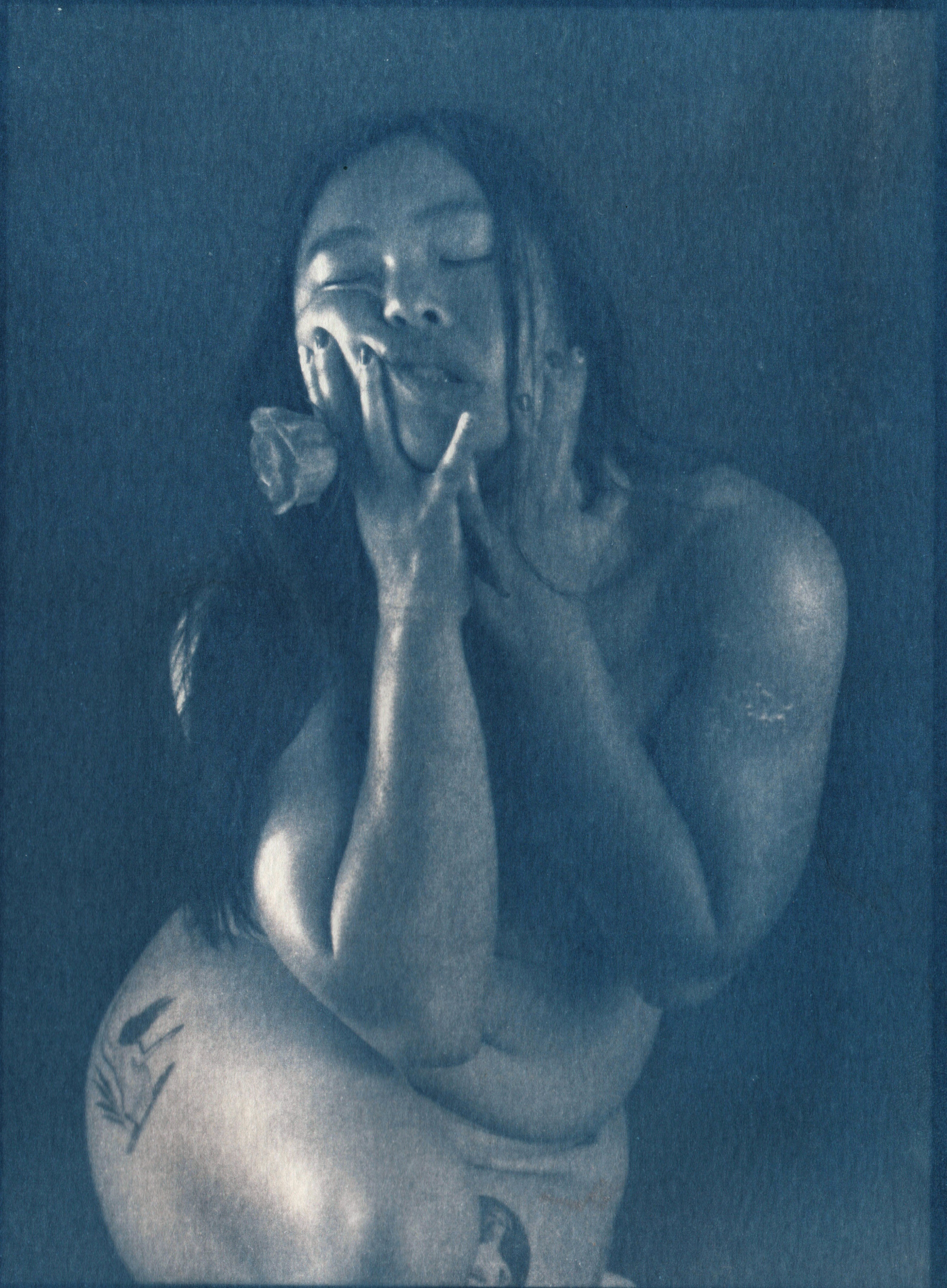 Cyanotype print of Lorraine with eyes closed, hands cupped around her face, holding a rose