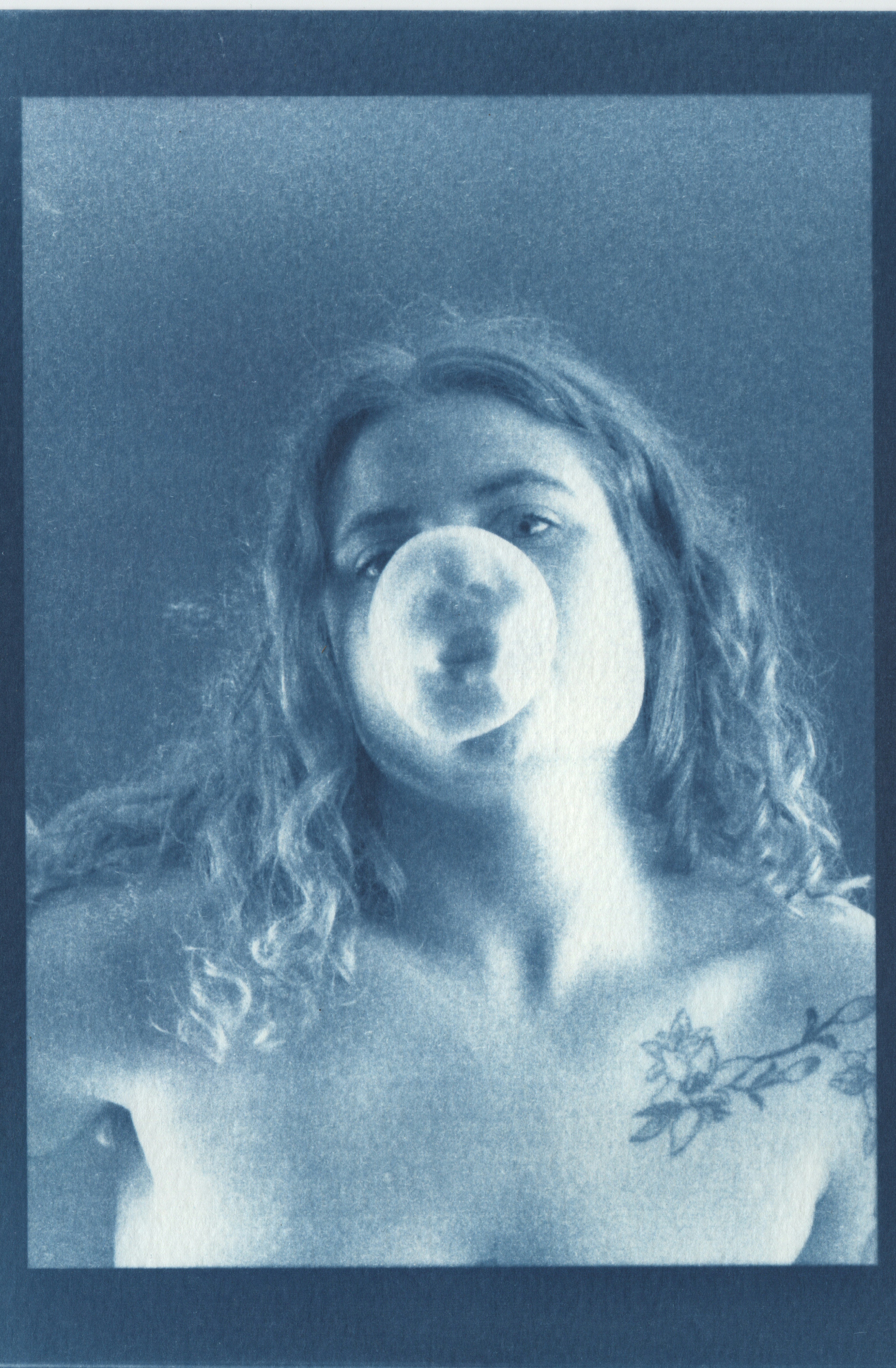 Cyanotype print of Maddie blowing a bubble, with a floral shoulder tattoo
